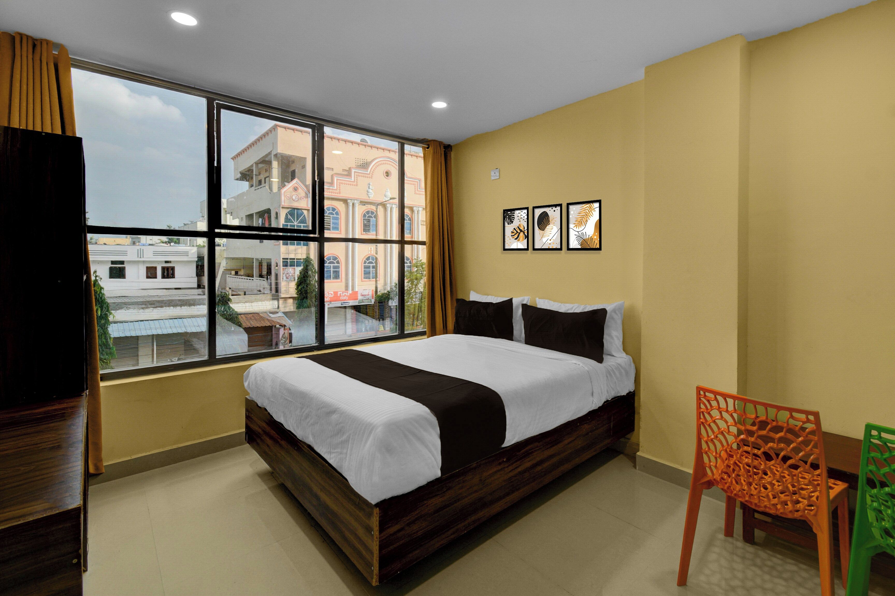 A hotel room with a large bed, a view of buildings outside, and a wall with framed pictures.