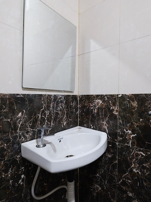 A bathroom with a white pedestal sink, a mirror above it, and dark marble walls. - Hotel O Nova Comfort Inn (Hyderabad)