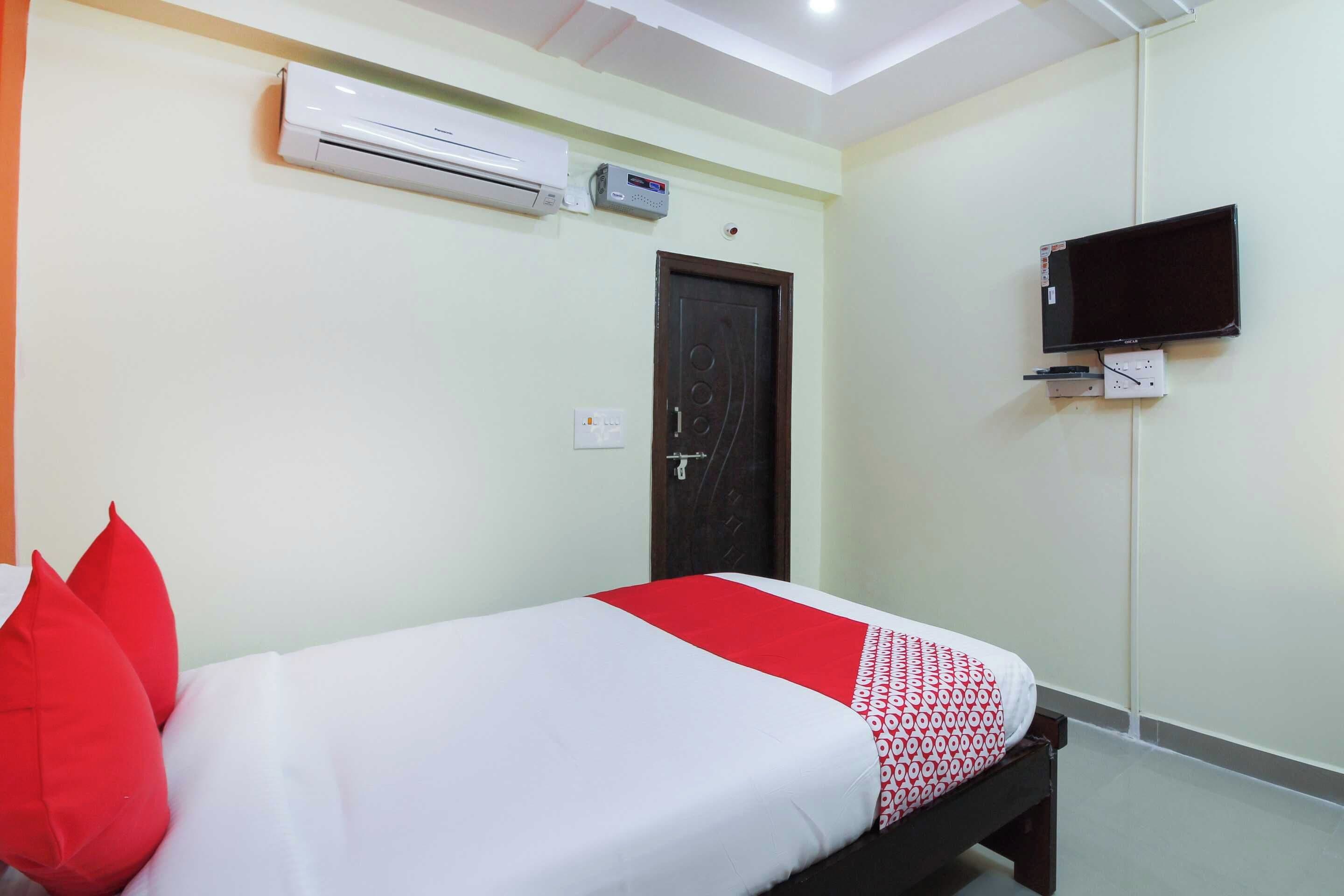 Habitación de hotel con una cama, un televisor montado en la pared y un equipo de aire acondicionado sobre la cama.