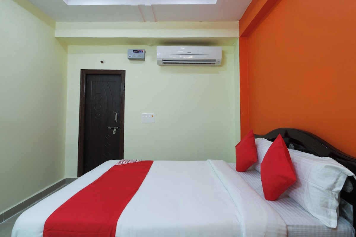 A hotel room with a bed, a door, an air conditioning unit, and a wall-mounted thermostat.