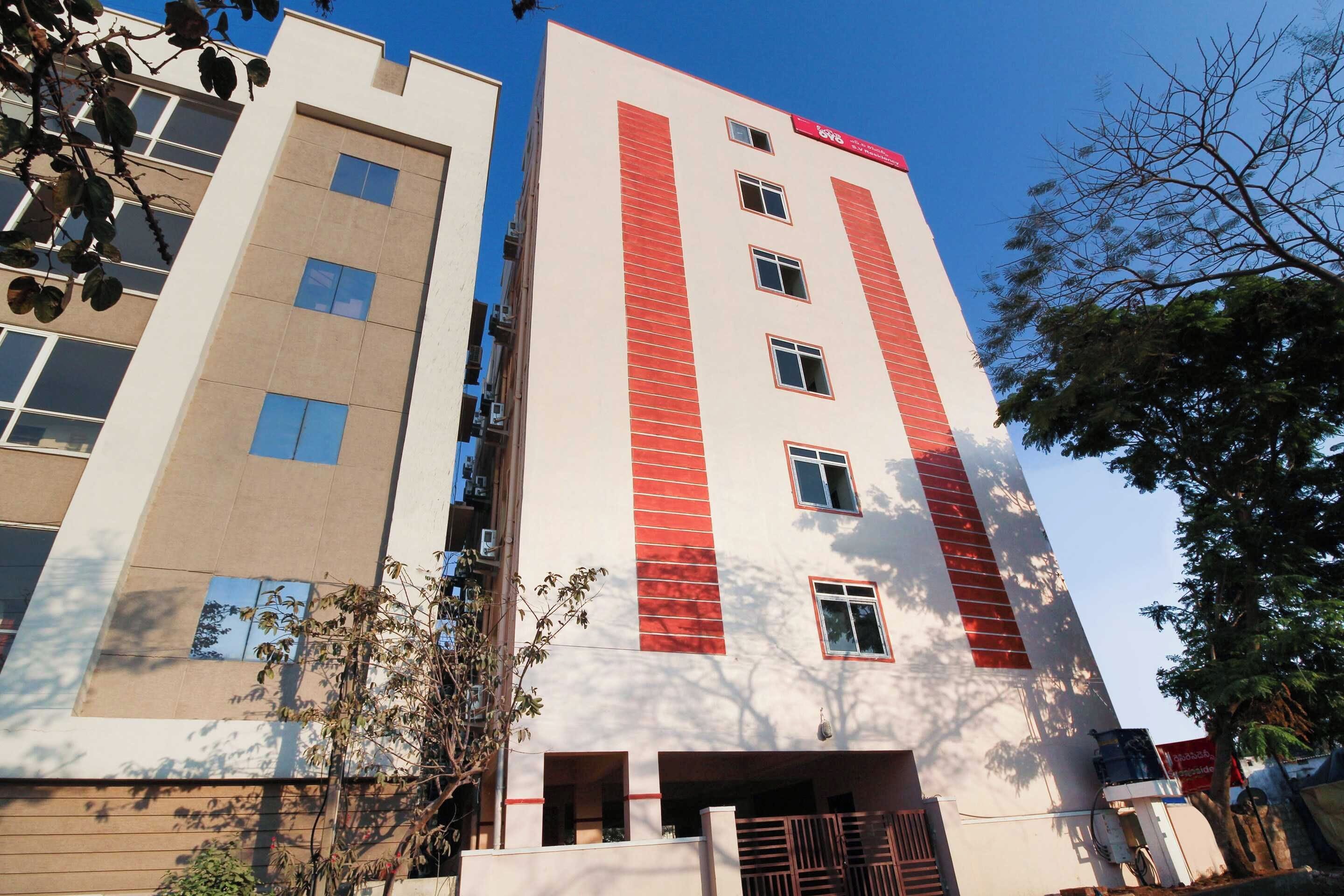 Un edificio de varios pisos con fachada roja y blanca, numerosas ventanas y una entrada visible.