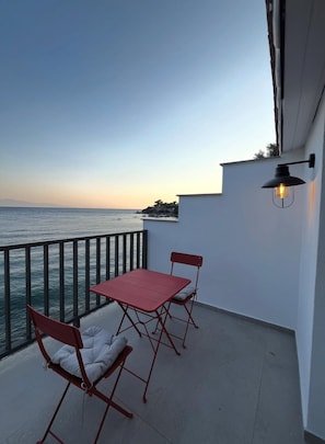 Un balcon avec une table et des chaises, donnant sur une étendue d’eau et une côte lointaine.