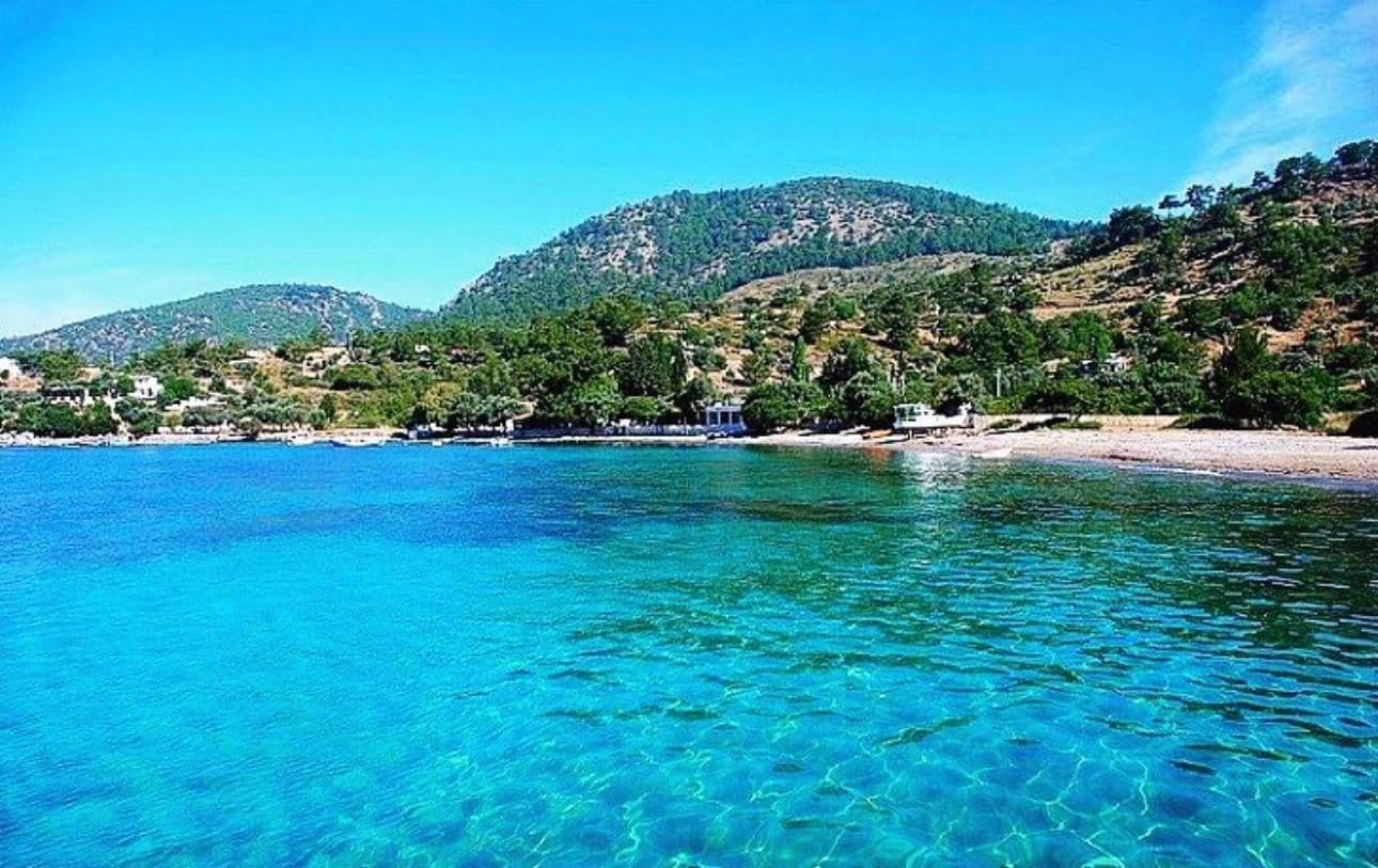 A coastal landscape with clear blue waters, a sandy beach, and a hilly backdrop.