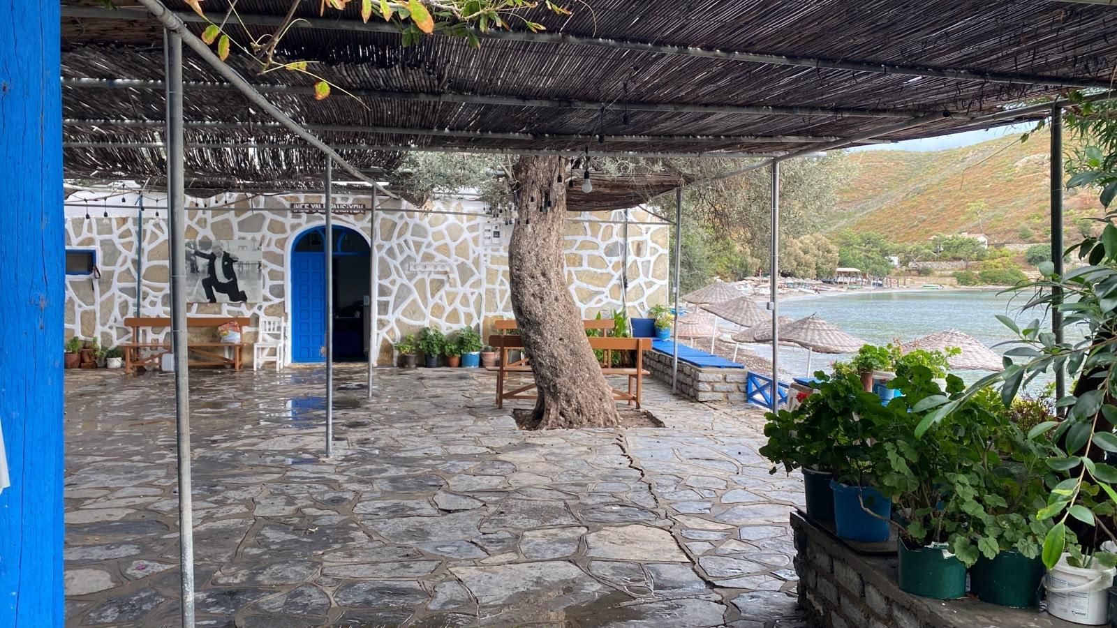 A stone-paved patio with a blue door, outdoor seating, and a view of a body of water.