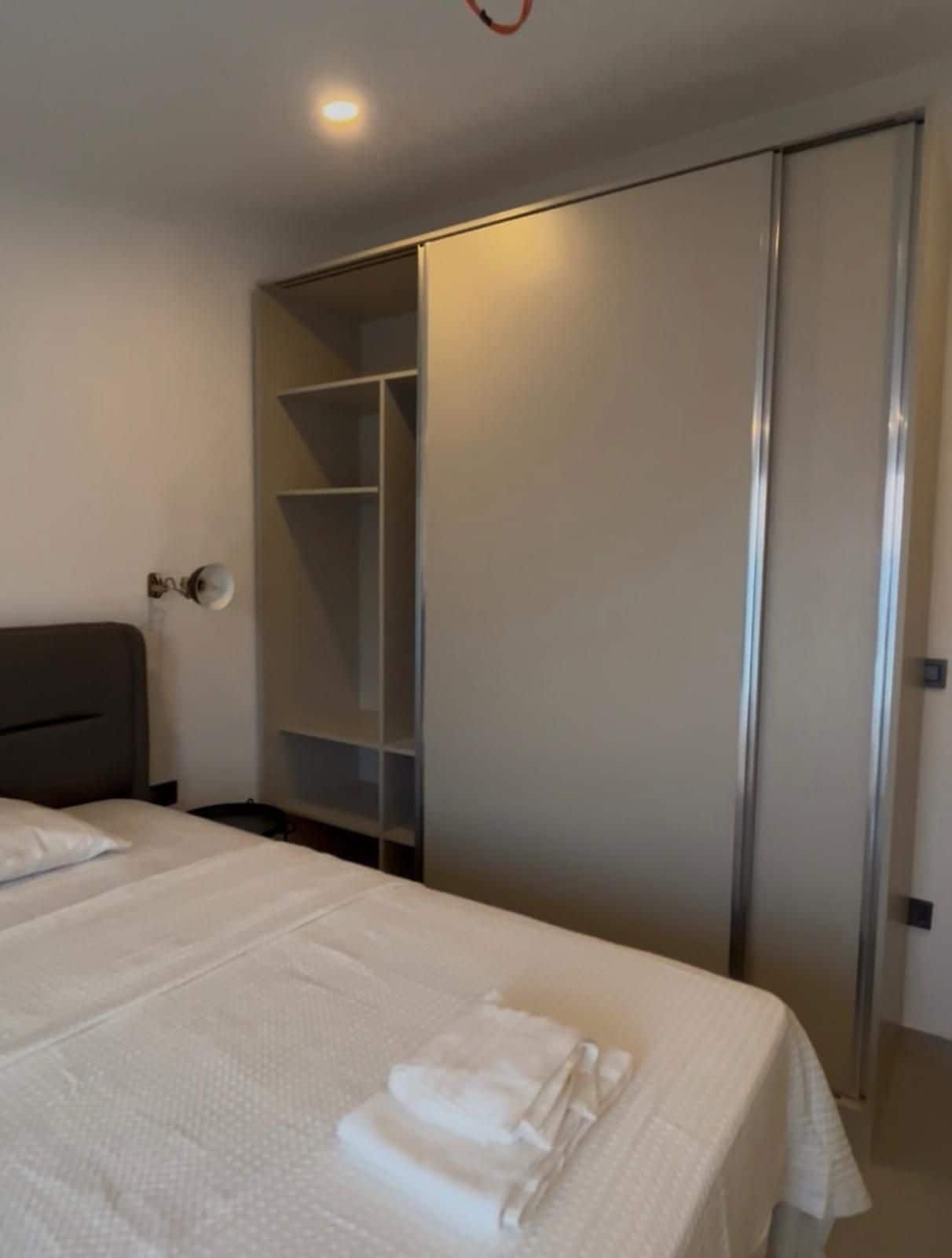 A hotel room with a bed, a wardrobe, and a bedside table.