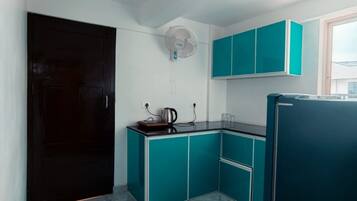 Una cocina compacta con armarios color turquesa, un refrigerador negro y un ventilador de techo blanco.