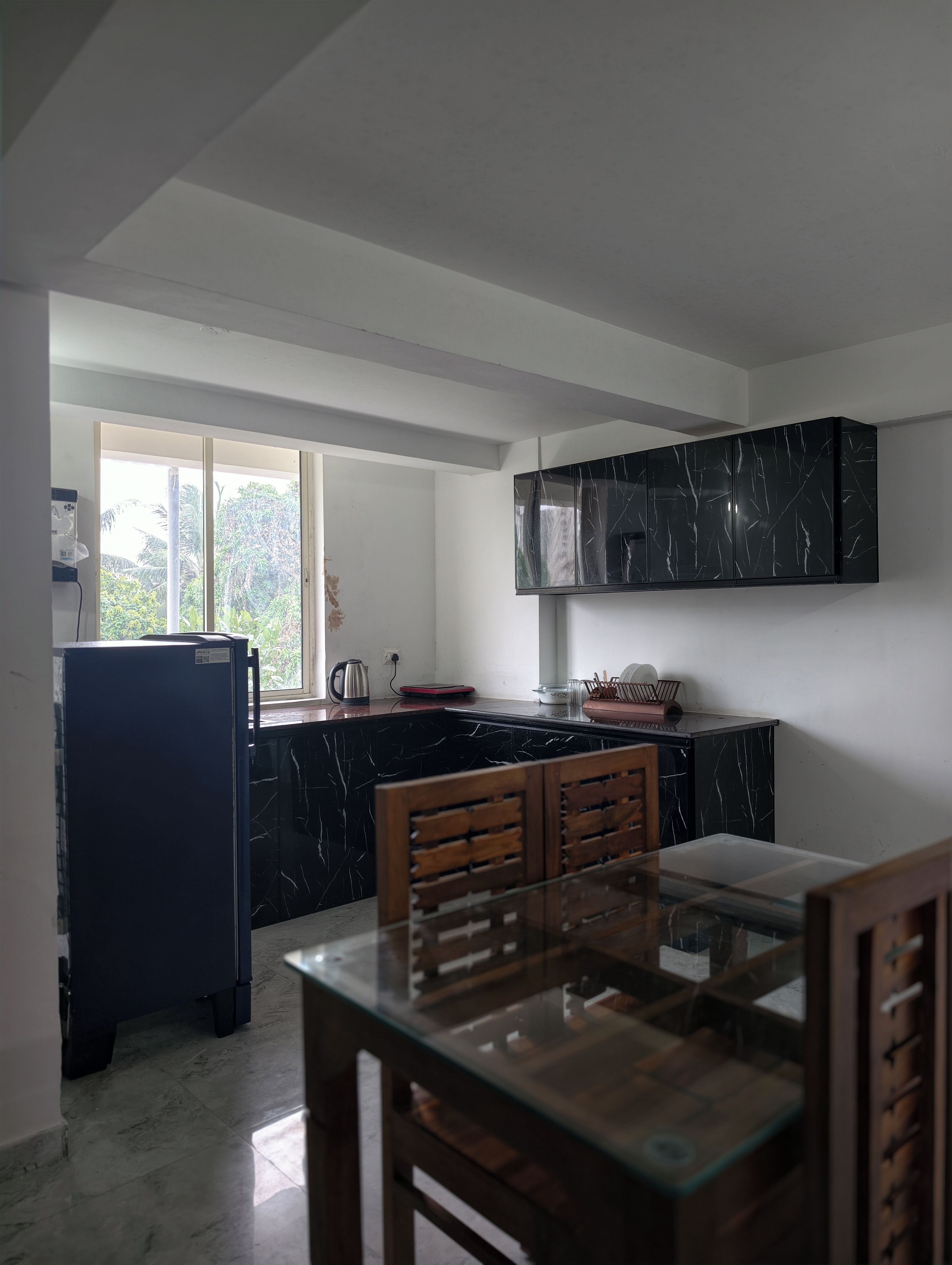 A kitchen with a black marble countertop, a refrigerator, and a wooden dining table.