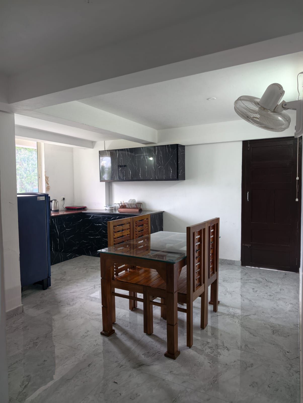 A dining area with a wooden table and chairs, a black marble kitchen island, a mounted TV, and a ceiling fan.