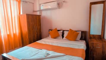 Et soveværelse med seng, træsenggavl, orange puder, et natbord, et klædeskab og en aircondition.