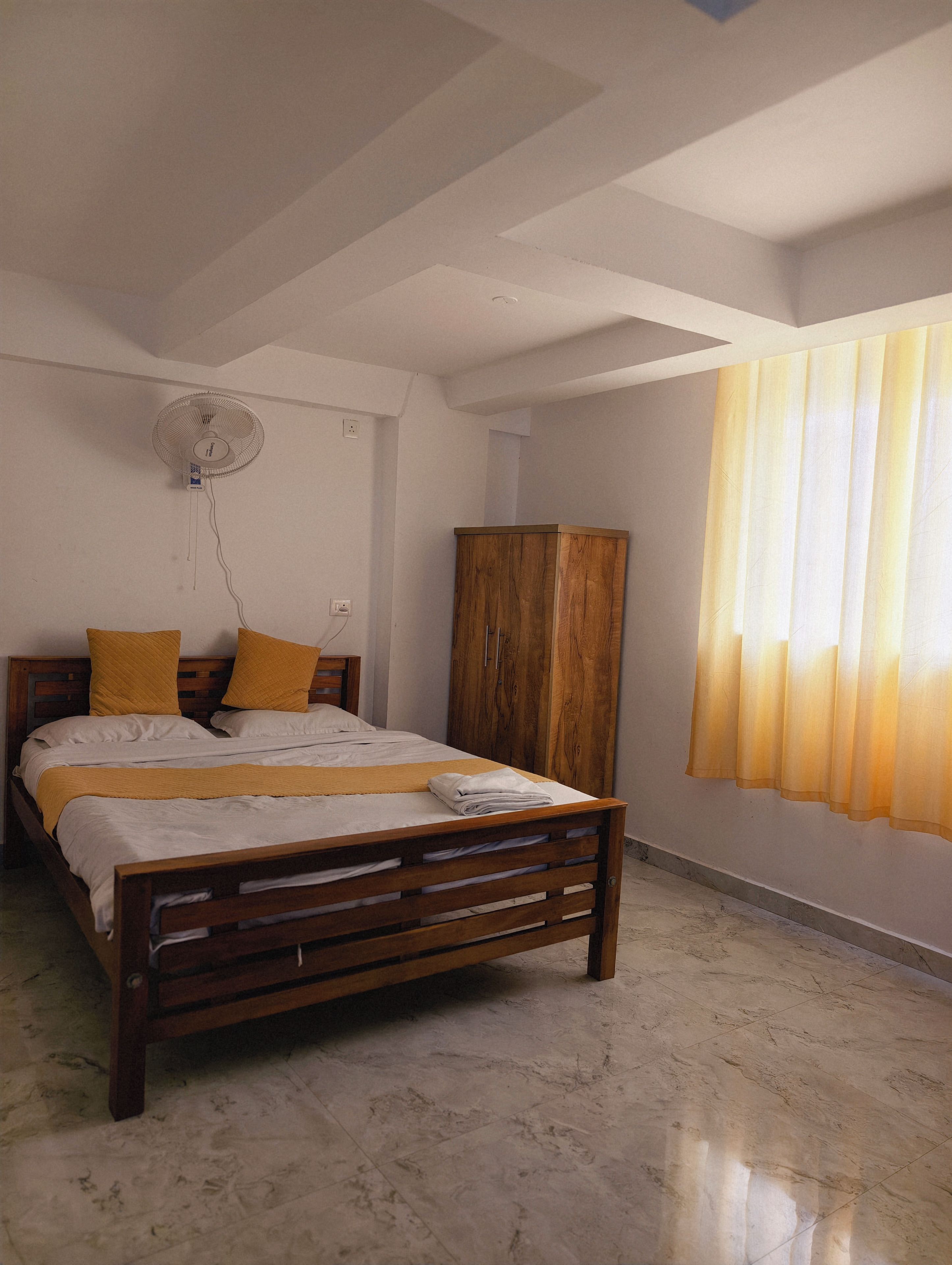 Un dormitorio con cama, armario de madera, ventilador de techo y ventana con cortinas.