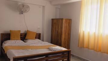 Un dormitorio con cama, armario de madera, ventilador de techo y ventana con cortinas.