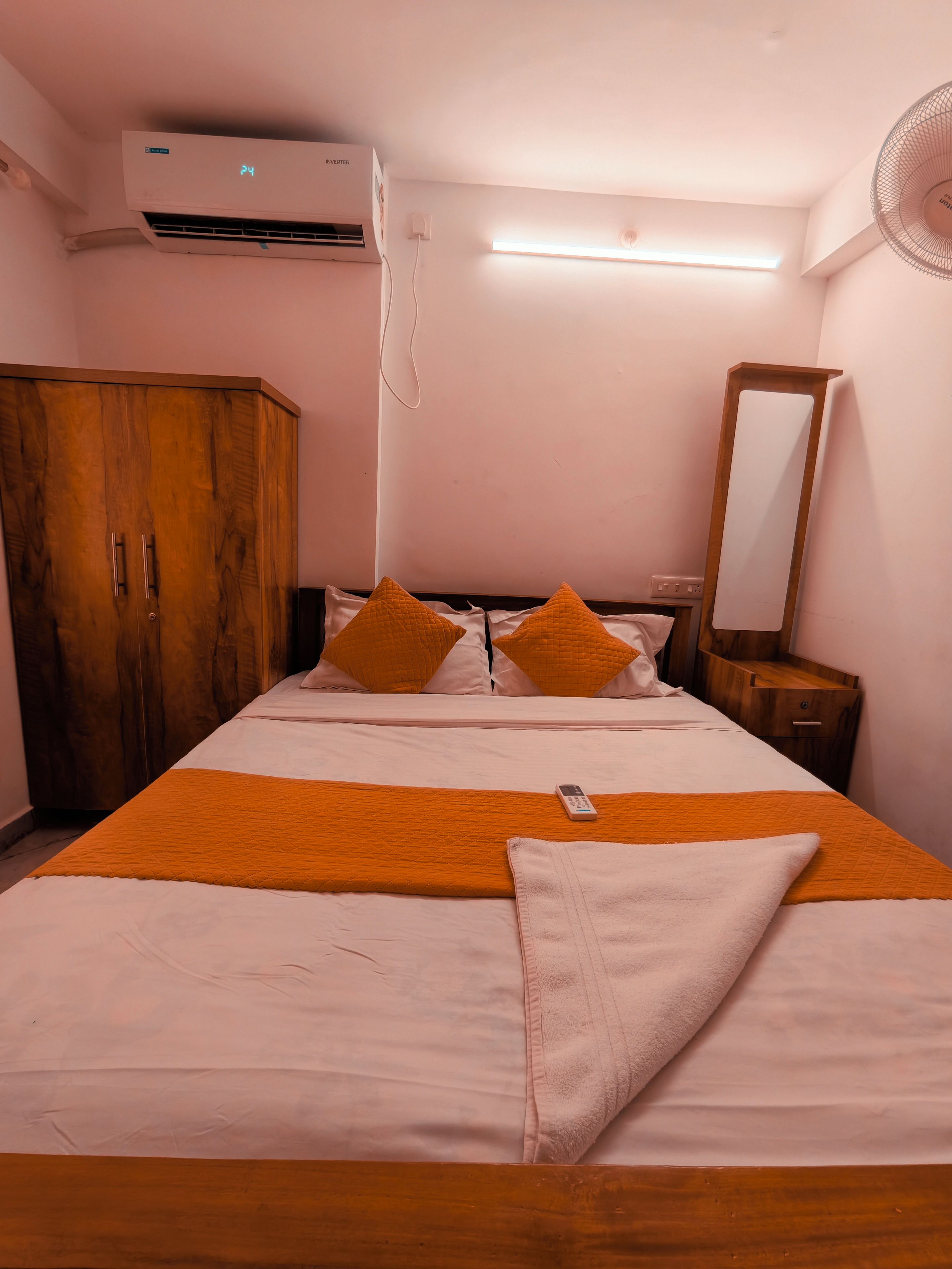 A hotel room with a bed, a wardrobe, a bedside table, a mirror, and an air conditioning unit.