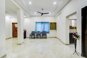 A spacious room with a ceiling fan, a dining area with chairs, a blue curtain, and a flower arrangement. - Hotel O RR GRAND STAY (Hyderabad)