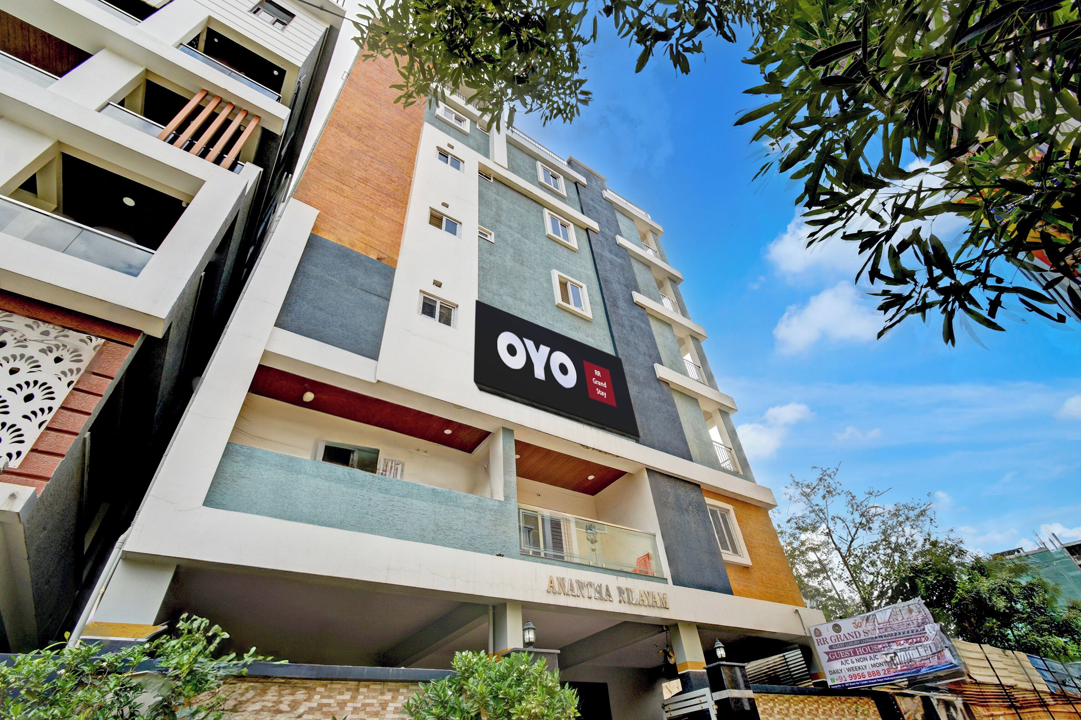 A multi-story building with balconies, a sign for 'OYO', and a sign for 'Anantha Neliavum'.