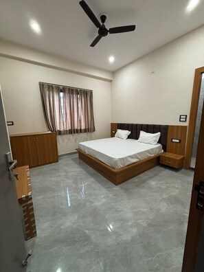 Un dormitorio con cama, ventilador de techo, armario, ventana con cortinas y puerta.