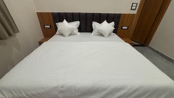 Una habitación de hotel estándar con una cama individual, dos almohadas, un cabecero y una mesita de noche.