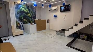 A hotel lobby with a reception desk, a staircase, and a mural of a forest.