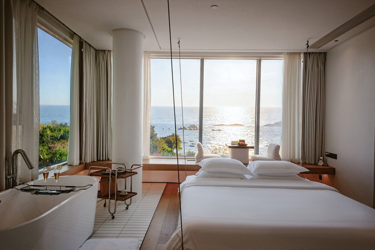 Ein Hotelzimmer mit einem großen Bett, einer Badewanne und Meerblick.
