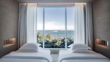 Quarto com duas camas, uma janela grande com cortinas e vista para o mar.