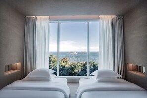 Ein Schlafzimmer mit zwei Betten, einem großen Fenster mit Vorhängen und Meerblick.