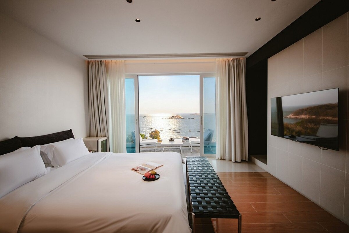Ein Hotelzimmer mit einem großen Bett, einem Flachbildfernseher und einem Balkon mit Meerblick.