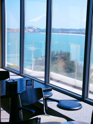 Ein Zimmer mit großen Fenstern und Blick auf eine Küstenlandschaft, inklusive Tisch und Stühlen.