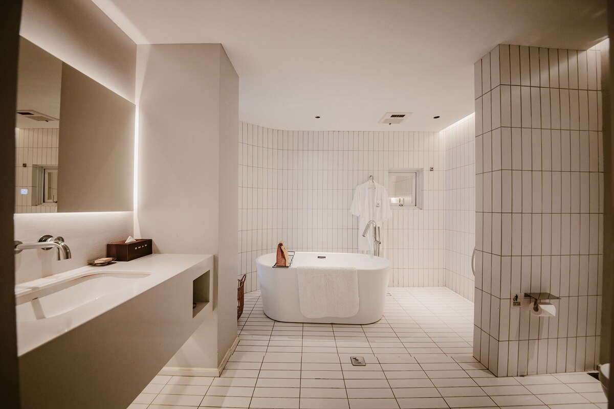 Ein modernes Badezimmer mit einer freistehenden Badewanne, einem großen Spiegel und einem Waschtisch mit Handtuchhalter.