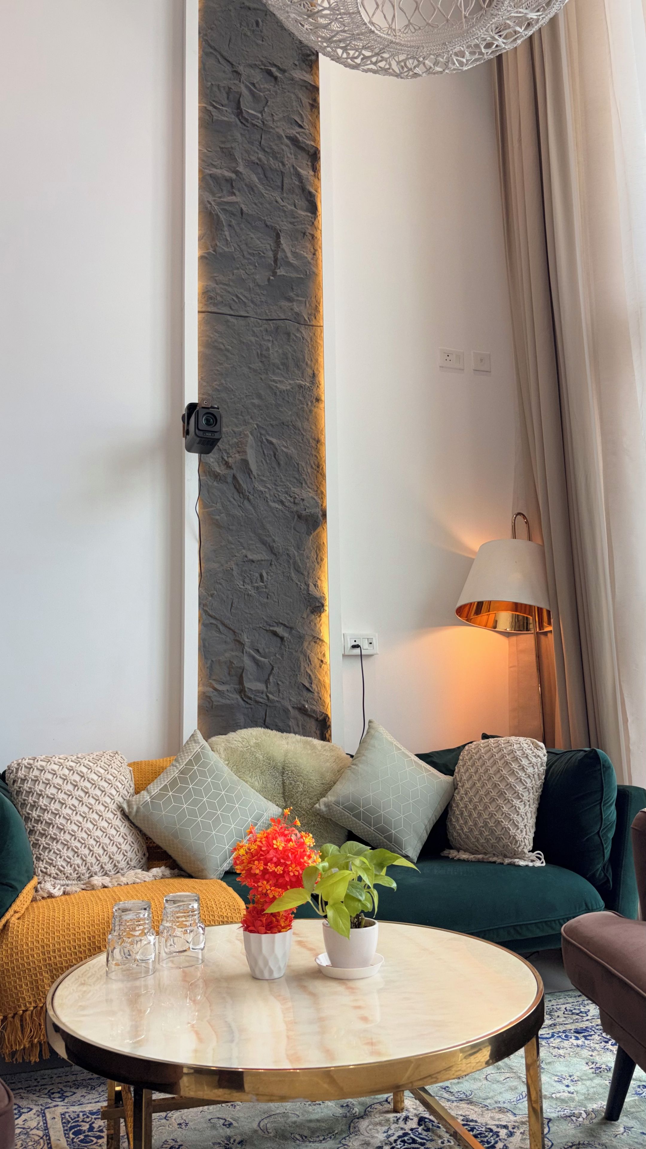 A modern living room with a stone accent wall, a round coffee table with glasses, a potted plant, and a lamp.