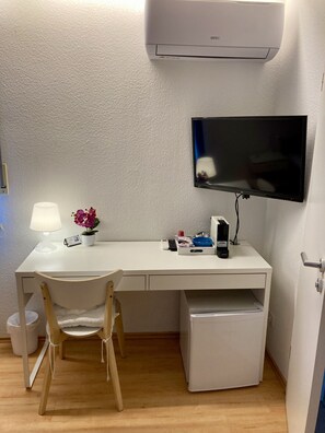 Pieni, siisti huone, jossa on työpöytä, tuoli, televisio ja valkoinen ilmastointilaite.