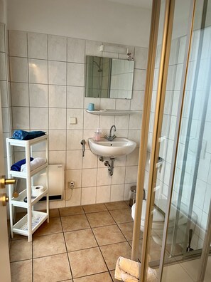 Une salle de bain avec un lavabo blanc, un miroir, une étagère avec des serviettes et un espace douche.