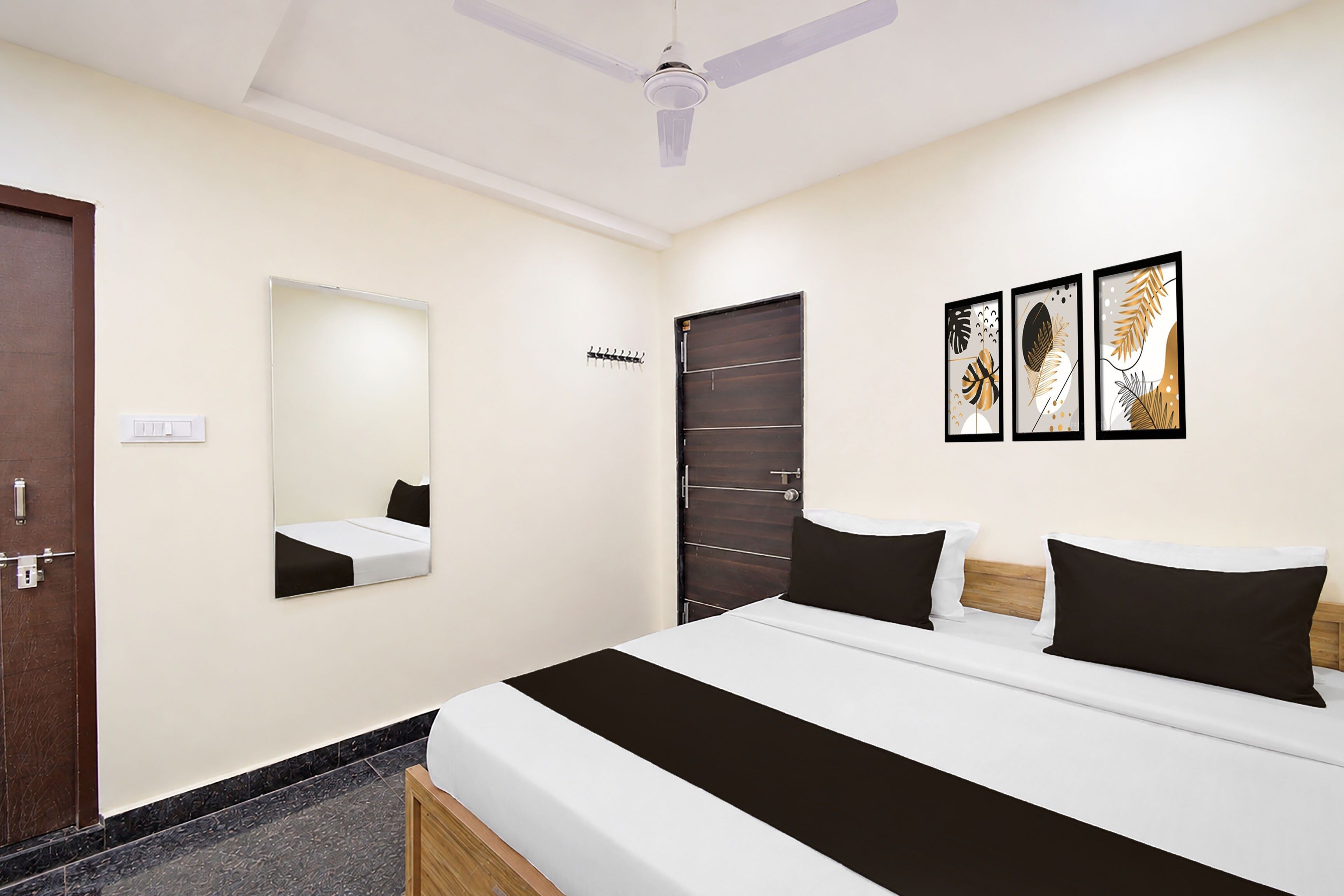 A hotel room with a bed, a mirror, a door, and three framed artworks on the wall.