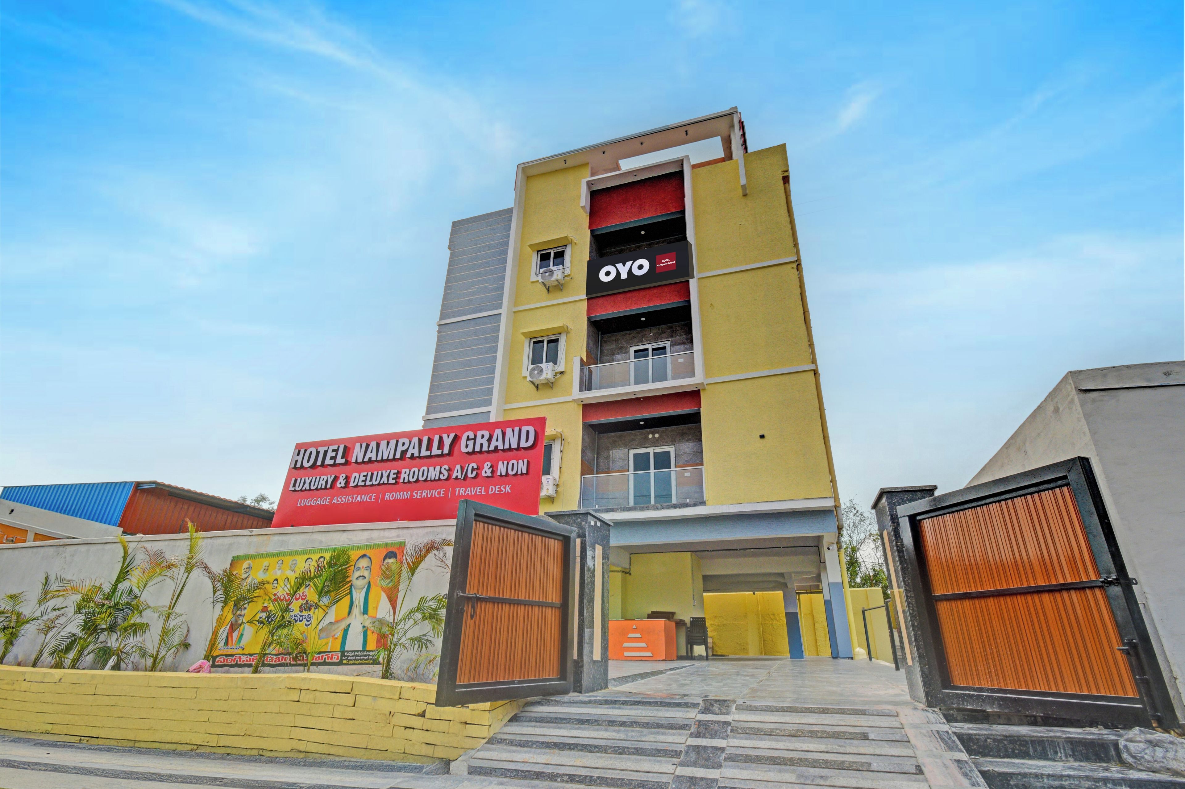 Un hotel de varios pisos con una fachada llamativa de color rojo y amarillo, que muestra un cartel con la leyenda 'Hotel Namphally Grand' y la marca 'OYO'.