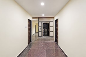 A hallway with a dark wooden door at the end, a light-colored wall, and a tiled floor. - Hotel O Nampally Grand (Hyderabad)