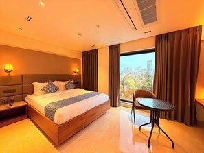 A hotel room with a large bed, a bedside table, a chair, and a view of the cityscape. - Palette Hotel Maneraa by CheckIn (Tirupati)