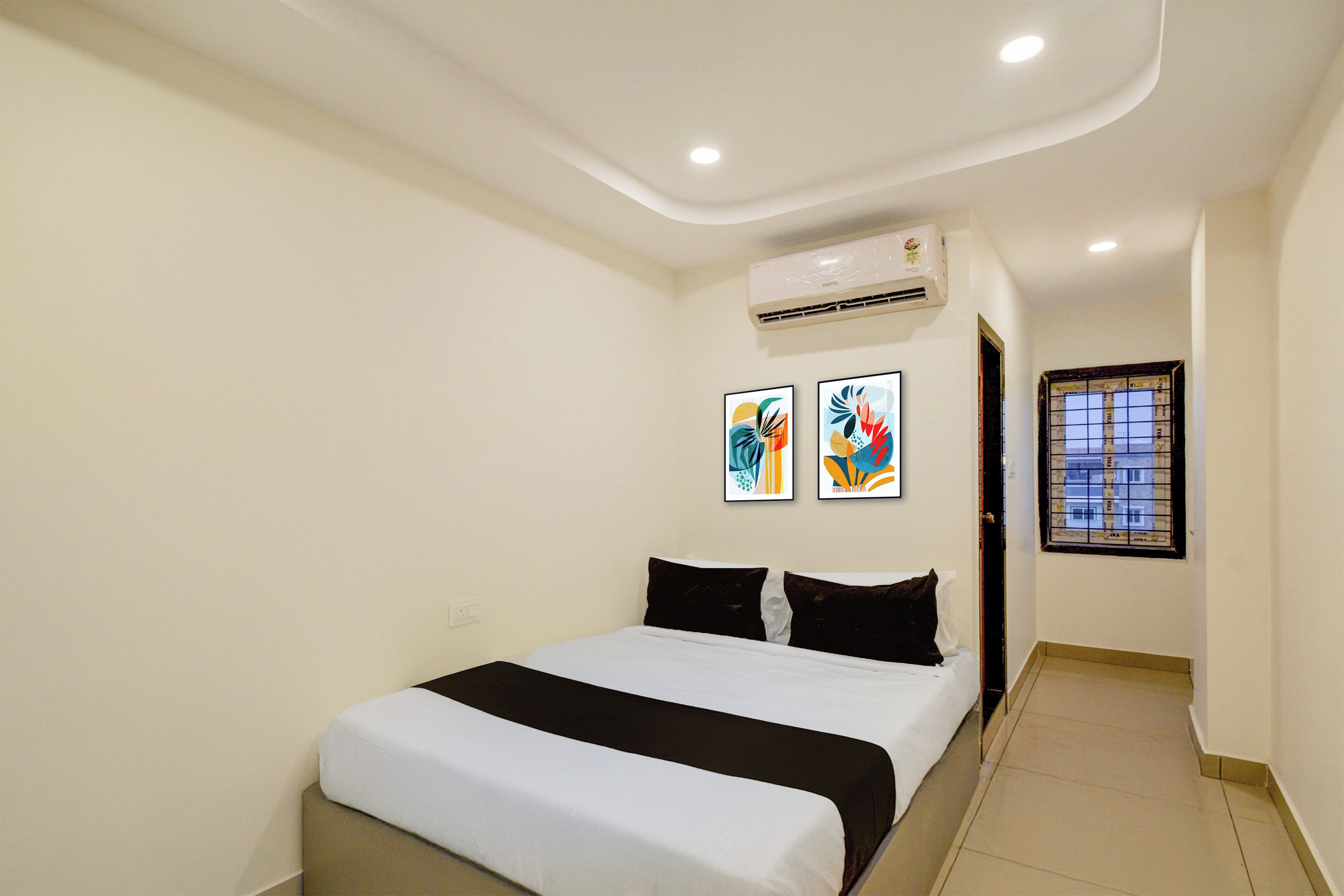 Una habitación de hotel con una cama, dos unidades de aire acondicionado fijadas a la pared y dos obras de arte enmarcadas.