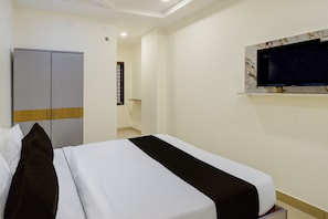 Una habitación de hotel con una cama, un armario, un televisor montado en la pared y un ventanal.