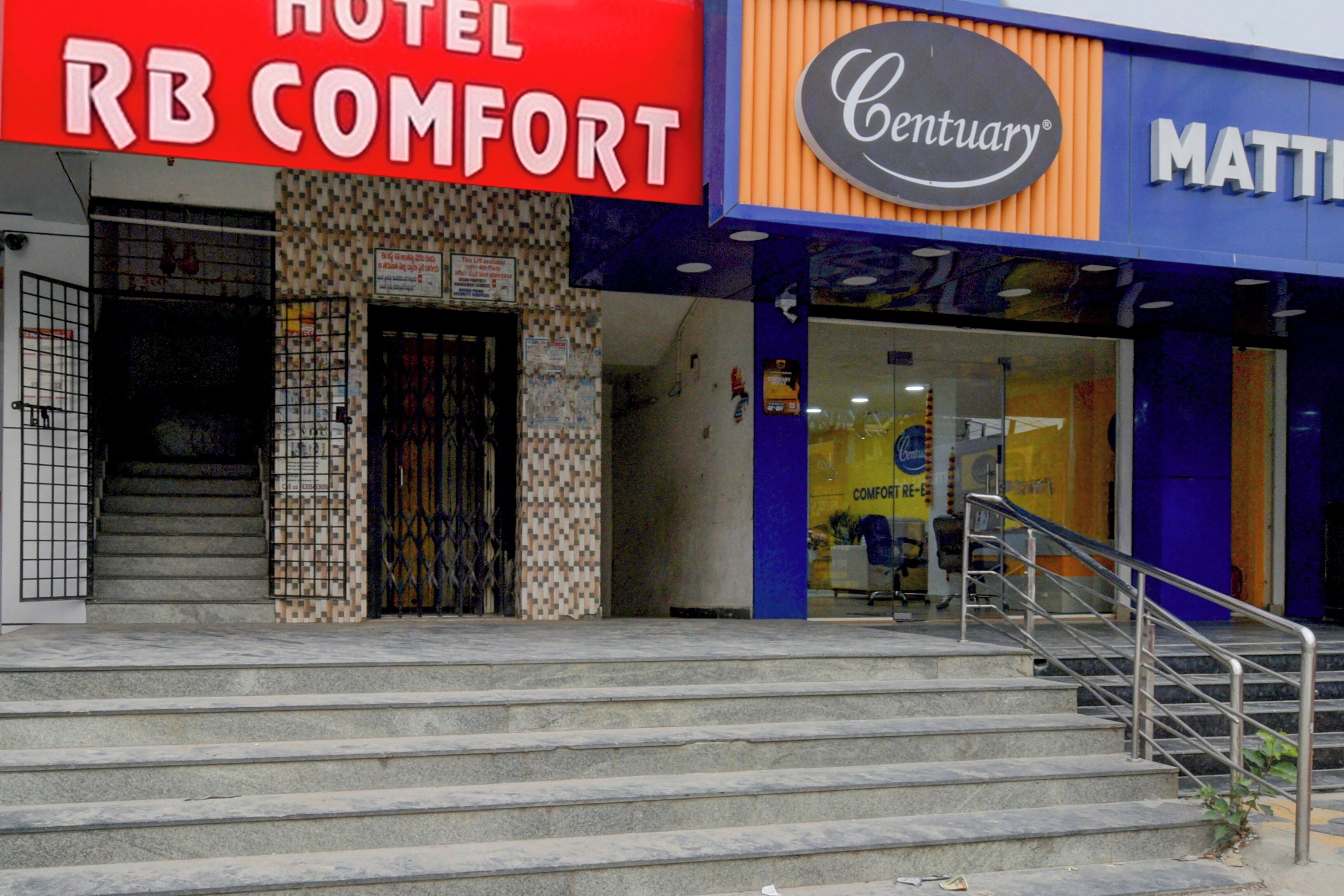 Entrada de un hotel con una escalera que lleva a la puerta, un letrero que dice 'Hotel RB Comfort' y un letrero 'Century' sobre la entrada.