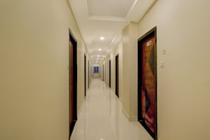 A hotel corridor with doors on both sides, a tiled floor, and a blue window at the end. - Hotel O RB Comfort (Hyderabad)