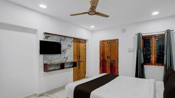 A bedroom with a bed, a ceiling fan, a TV mounted on a marble wall, wooden wardrobes, and a window with curtains.