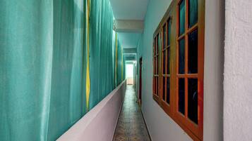 A corridor with a tiled floor, a white wall, and a window with a wooden frame.