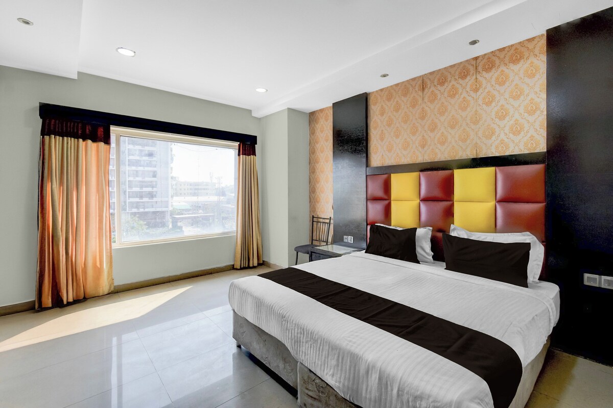 A hotel room with a large bed, a window with curtains, a headboard with a patterned design, and a tiled floor.
