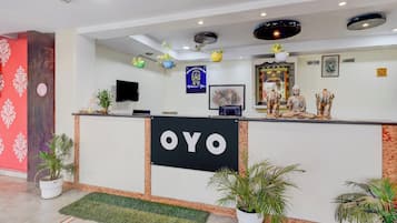 A hotel reception desk with a sign reading 'OYO', a flat-screen TV, a framed welcome sign, and a Buddha statue.