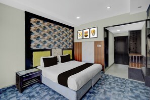 Una habitación de hotel moderna con una cama grande, una mesita de noche, un panel decorativo en la pared y una obra de arte enmarcada sobre la cama.