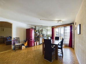Un salón amplio con mesa de comedor, sillas, sofá, un refrigerador rojo y una cocina al fondo.
