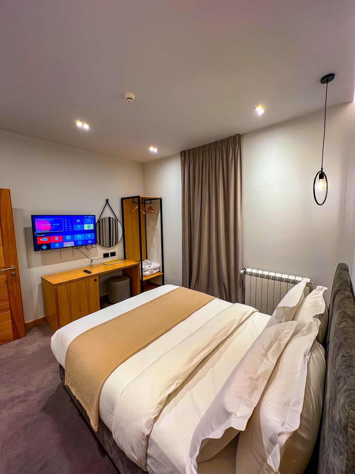 A modern hotel room with a large bed, a desk with a computer, a television, and a radiator.