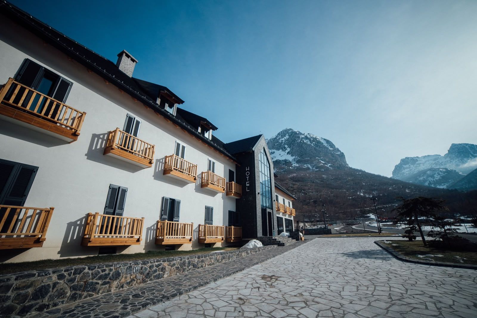 Un hotel con varios balcones, un patio empedrado y montañas al fondo.