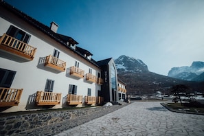 A hotel with multiple balconies, a stone-paved courtyard, and a mountain backdrop. - Hotel Kulla e Bajraktarit (Shkrel)