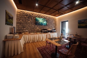 Espaço de refeições com parede de pedra, TV de tela plana, sistema de buffet e tapete estampado.