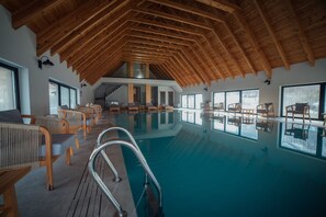 An indoor swimming pool with wooden beams, lounge chairs, and large windows. - Hotel Kulla e Bajraktarit (Shkrel)