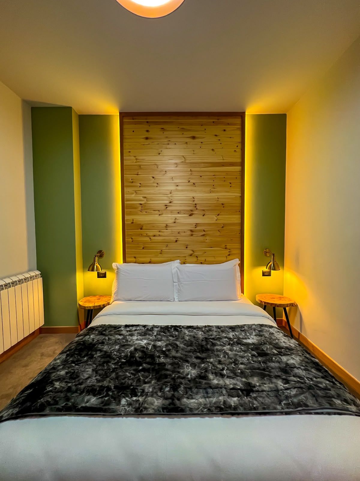 Un dormitorio con una cama, dos mesitas de noche, un radiador y un cabecero de madera.